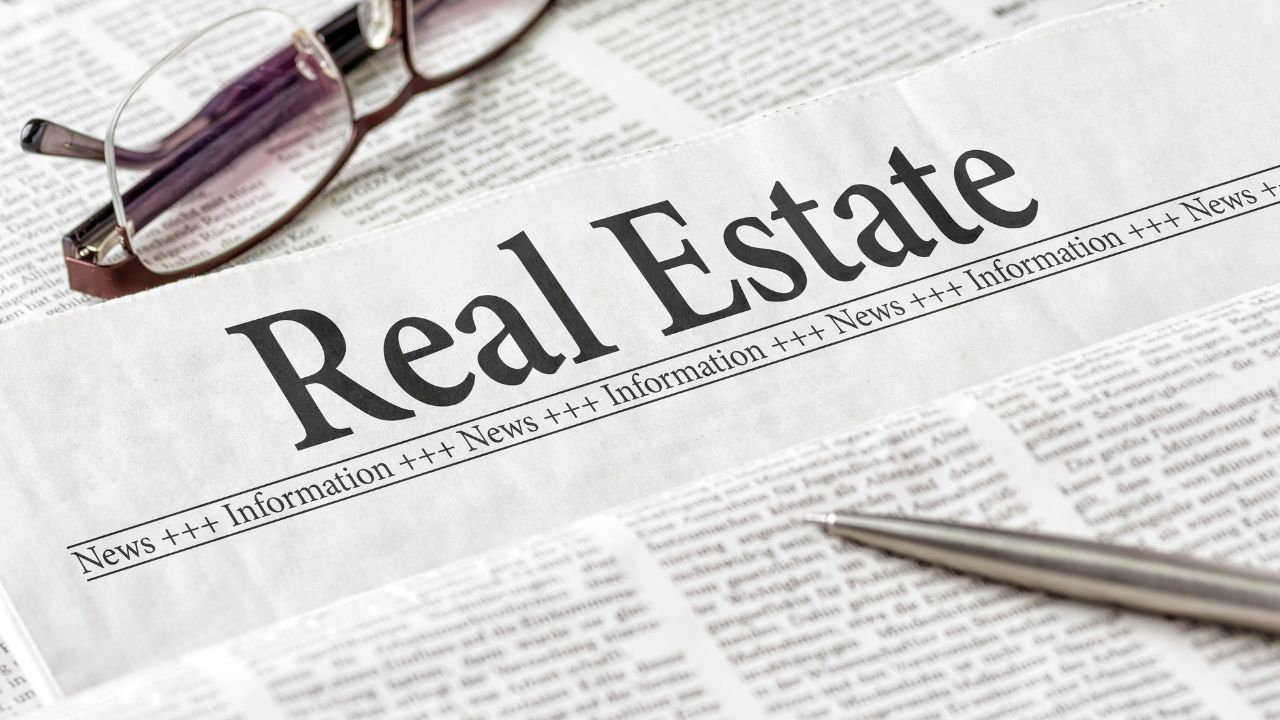 Glasses and a pen set on top of a newspaper page with the title "Real Estate"